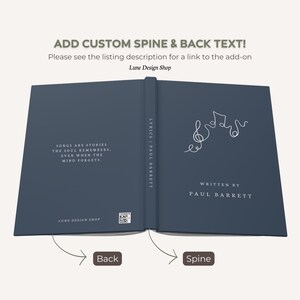 May include: Open book with a dark blue cover. The left page has text that reads "SONGS ARE STORIES, THE SOUL REMEMBERS, EVEN WHEN THE MIND FORGETS." The right page has musical notes and the text "WRITTEN BY PAUL BARRETT."