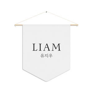 May include: White fabric banner with the name LIAM and the Korean translation written in black lettering. The banner is hanging from a wooden dowel rod with string.