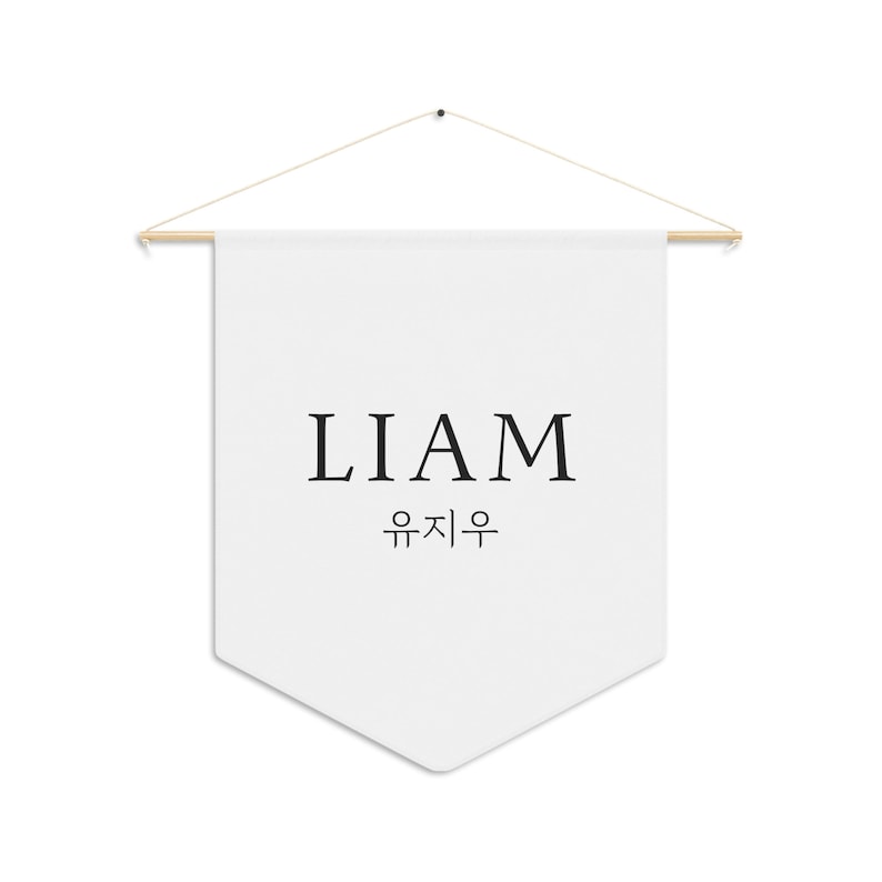 May include: White fabric banner with the name LIAM and the Korean translation written in black lettering. The banner is hanging from a wooden dowel rod with string.