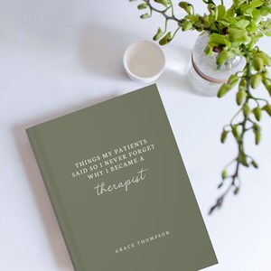 May include: A sage green journal with the text "THINGS MY PATIENTS SAID SO I NEVER FORGET WHY I BECAME A therapist" and the author's name, Grace Thompson. A small white cup and a glass vase with green plants are also visible.
