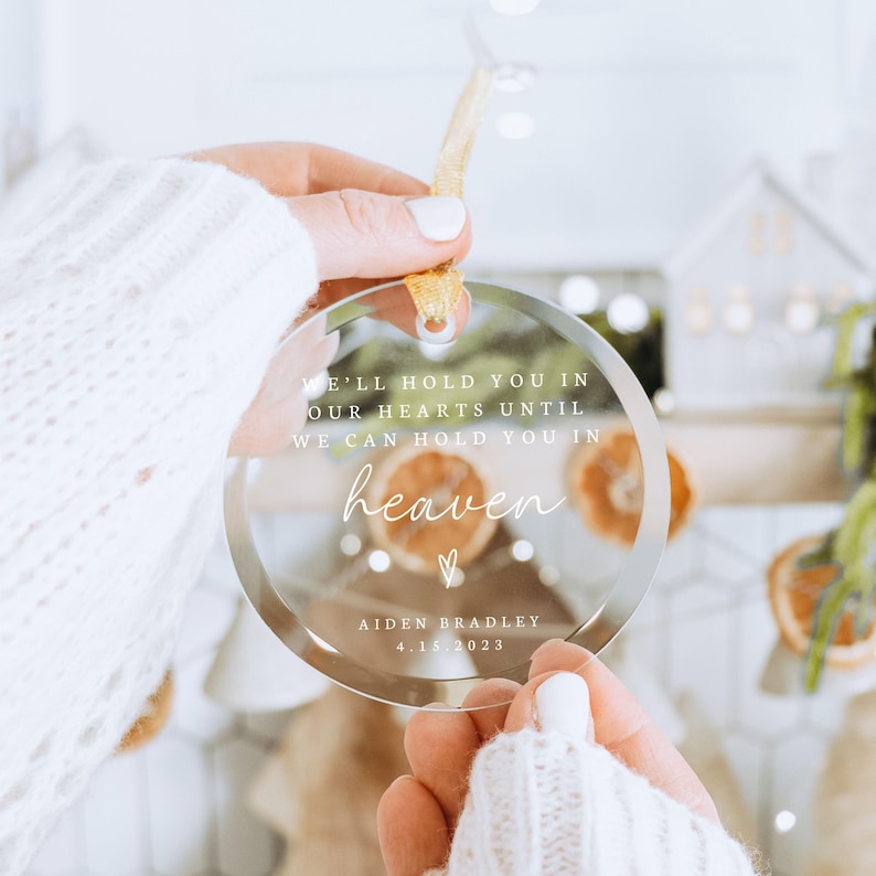 May include: A clear glass ornament with the text "WE'LL HOLD YOU IN OUR HEARTS UNTIL WE CAN HOLD YOU IN heaven" and "AIDEN BRADLEY 4.15.2023".