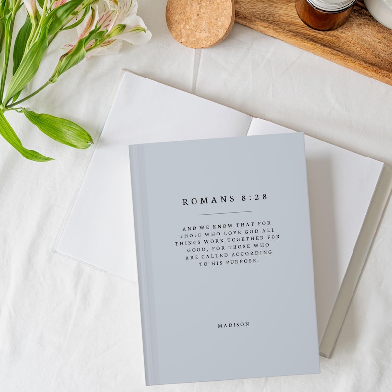 May include: A light blue journal with the text "Romans 8:28" and the quote "And we know that for those who love God all things work together for good, for those who are called according to His purpose." The journal also has the word "Madison" printed on the bottom.