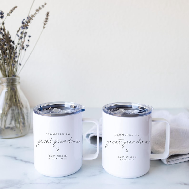 May include: Two white ceramic mugs with black text that reads "Promoted to Great Grandma" with a heart symbol and the baby's name and birthdate. The mugs have a stainless steel lid and a handle.
