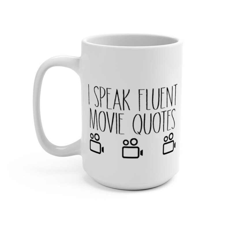 May include: White ceramic coffee mug with a black design that says "I speak fluent movie quotes" with three black film camera icons.