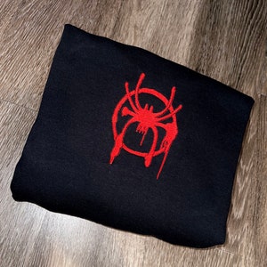 Puede incluir: Sudadera negra con un logotipo de Spider-Man bordado en rojo.
