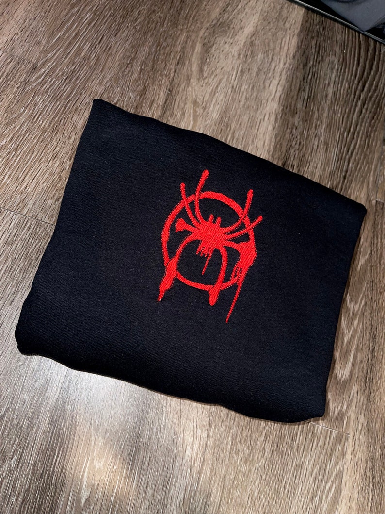 Puede incluir: Sudadera negra con un logotipo de Spider-Man bordado en rojo.