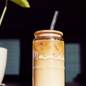 May include: A clear glass jar with a bamboo lid and a straw filled with iced coffee. The jar has the text "Maman" and "Olivia, Nathan et" written on it.