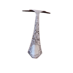 May include: A silver serving spoon with an ornate design of grapevines and leaves. The handle is shaped like a teardrop and has a hexagonal base.