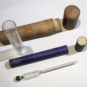 May include: A vintage medical thermometer with a glass bulb and a wooden case. The thermometer is in a protective case with a purple fabric lining. The case is made of wood and has a brown finish. The thermometer is used to measure body temperature.