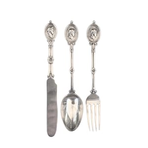 May include: A set of three silver-plated utensils with ornate handles featuring a profile of a person in a helmet. The set includes a knife, a spoon, and a fork.