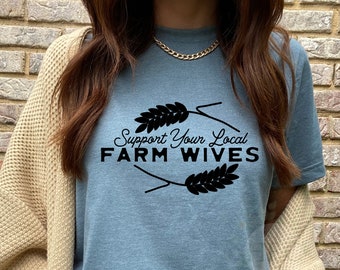 May include: A blue t-shirt with the text "Support Your Local FARM WIVES" in black lettering. The text is surrounded by two wheat stalks.