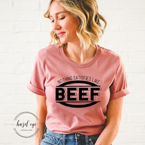 May include: A pink t-shirt with a black graphic that says "Nothing satisfies like BEEF" in a circle.