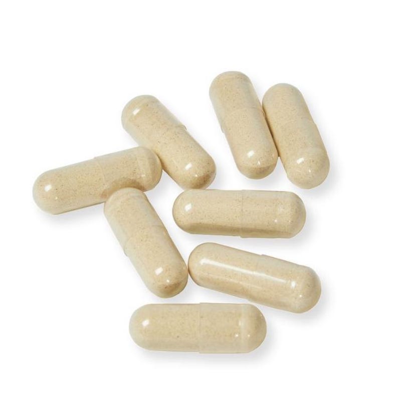 May include: A group of eight beige capsules, scattered on a white background.