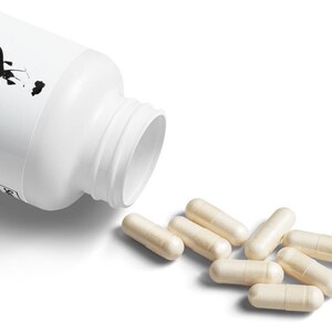 May include: A white plastic bottle with a black design on the label is open and spilling out beige capsules.