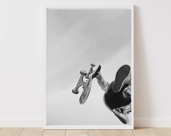 May include: Black and white framed print of a skateboarder mid-air. The skateboard is held in the air, with the skater's legs and shoes visible. The background is a plain, light sky.