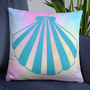 Op de afbeelding: Een decoratief kussen met een pastelroze, blauwe en gele ombre achtergrond. Een turquoise blauwe schelp met witte strepen is gecentreerd op het kussen.