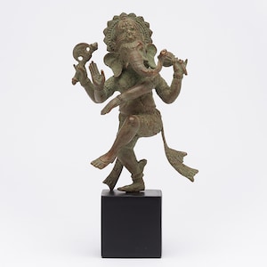 Puede incluir: Estatua de bronce del dios hindú Ganesha, con cabeza de elefante y múltiples brazos, sobre una base cuadrada negra. La estatua está intrincadamente tallada y representa al removedor de obstáculos.