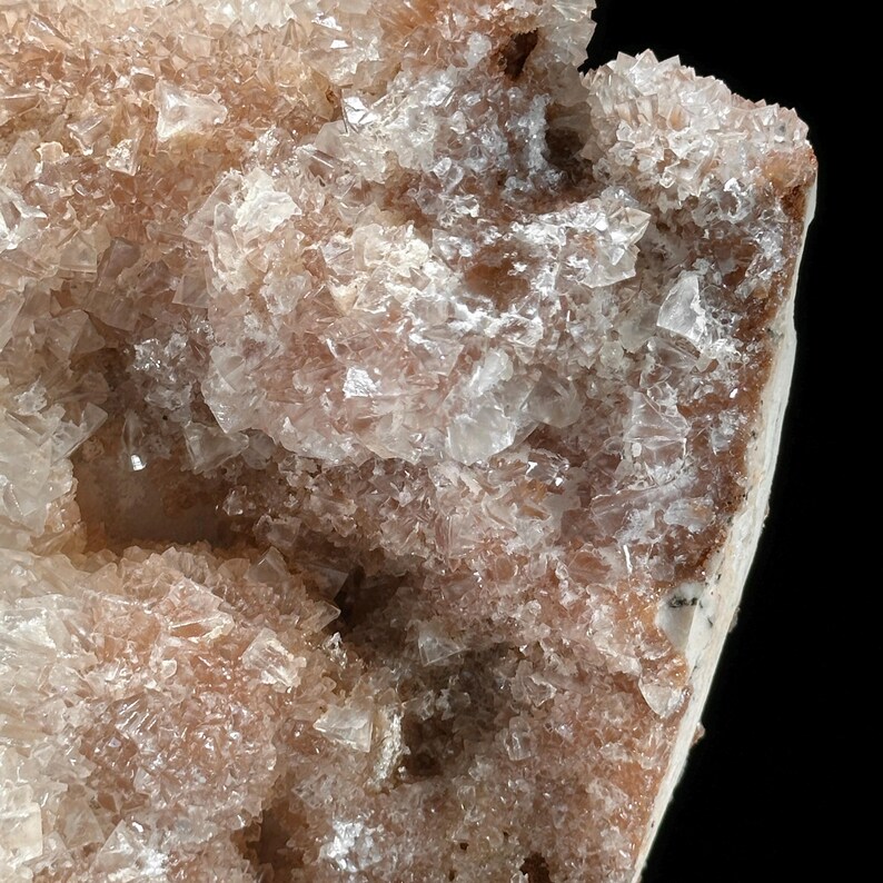 May include: Close-up of a mineral specimen with a crystalline structure. The crystals are a mix of translucent white and light brown, creating a textured, layered appearance. The background is black, highlighting the mineral's details.