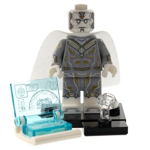 Pu&ograve; includere: Una minifigure in plastica bianca e grigia con accenti dorati, che indossa un mantello bianco traslucido. La figura poggia su una base nera accanto a un piccolo accessorio per console informatica blu chiaro con grafiche tecniche stampate e un elemento a nuvola in plastica trasparente.