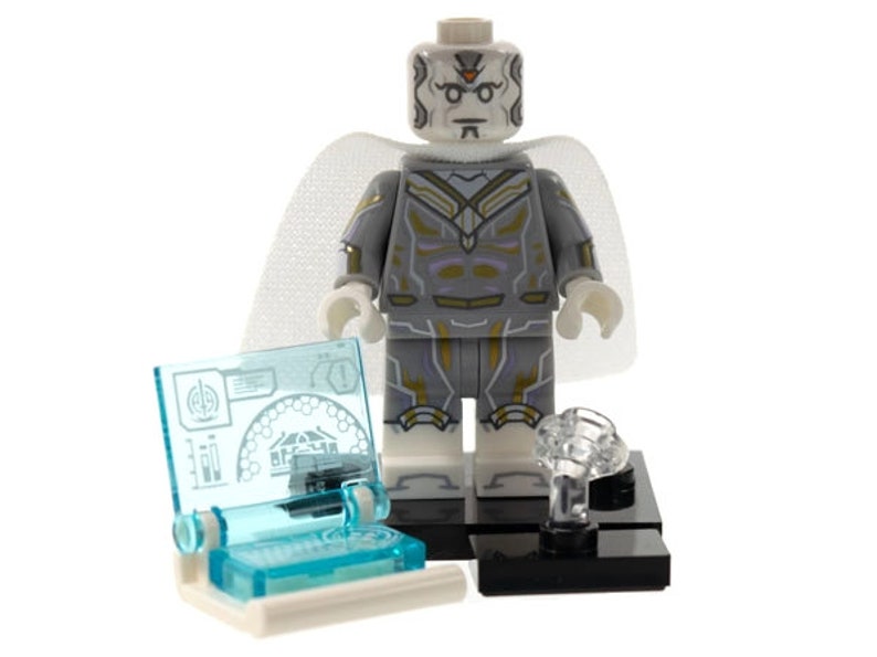 Pu&ograve; includere: Una minifigure in plastica bianca e grigia con accenti dorati, che indossa un mantello bianco traslucido. La figura poggia su una base nera accanto a un piccolo accessorio per console informatica blu chiaro con grafiche tecniche stampate e un elemento a nuvola in plastica trasparente.