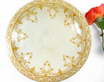 Op de afbeelding: Een witte keramische kom met een gouden bloemmotief rond de rand. De kom is rond en ondiep.