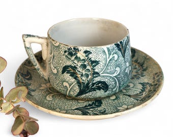 Op de afbeelding: Antieke kop en schotel set. De kop en schotel zijn versierd met een blauw en wit bloemmotief. De kop heeft een oor en staat op een bijpassende schotel. Een vintage set voor de thee.