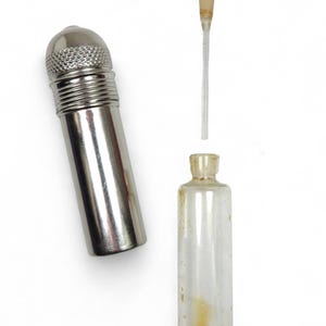 Peut inclure: Un flacon en métal argenté avec un bouchon à vis et un compte-gouttes en verre. Le flacon est vide et le compte-gouttes est transparent.