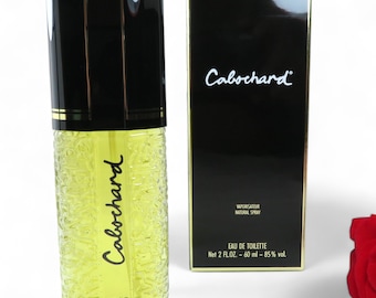 May include: A clear glass bottle of Cabochard Eau de Toilette by Gres Paris. The bottle is 2 fluid ounces and has a black cap. The bottle is sitting on a white surface.