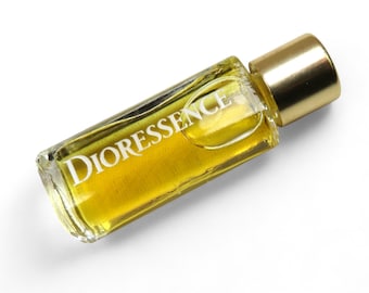 May include: A small, clear glass bottle with a gold cap. The bottle contains a yellow liquid and has the word "DIORESSENCE" printed on the label.