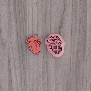May include: Two pink plastic cookie cutters shaped like a tongue with a mouth. The tongue is sticking out and has a grid pattern.