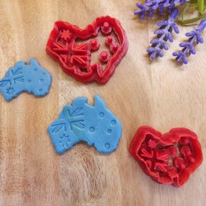 May include: Two blue and two red cookie cutters shaped like the outline of Australia with the Australian flag design. The cutters are on a wooden surface.