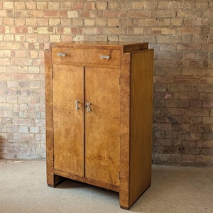 May include: A wooden cabinet featuring a light brown burl wood veneer finish. The piece includes one top drawer and two lower doors, all equipped with silver-toned metal hardware. The structure has a rectangular frame with a flat top surface.