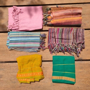 May include: Six different fabric scarves in various colours and patterns, including pink, blue, yellow, green, and brown. The scarves are folded and arranged on a wooden surface.