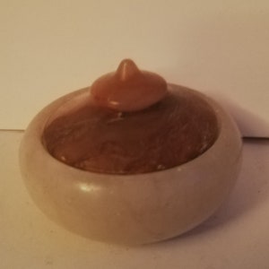 May include: A small, round, white alabaster trinket box with a brown lid. The lid has a pointed top and a swirling pattern.