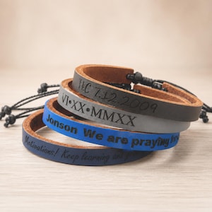 May include: A stack of four leather bracelets with adjustable black cord closures. The top bracelet is dark brown with "HC 7.12.2009" engraved. The second is grey with "VI•XX•MMXX". The third is blue with "Jonson We are praying for". The bottom is navy with "Motivations! Keep learning and grow".