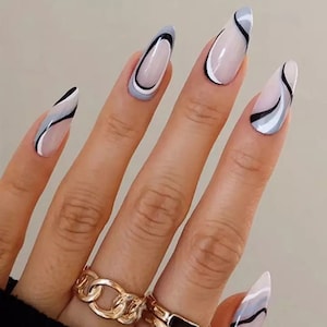 May include: A hand with long, pointed nails painted with a white, black, and gray abstract design. The nails are shaped like almonds and have a glossy finish.