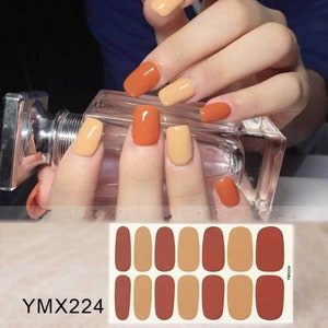 May include: A sheet of nail polish stickers with 12 individual stickers. The stickers feature two different colors: a light orange and a dark orange. The stickers are arranged in two rows of six. The text "YMX224" is printed on the sheet.