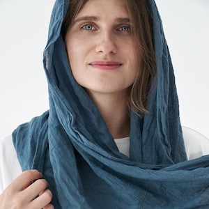 Może przedstawiać: Turkusowy szalik narzucony na głowę i ramiona. Szalik wykonany jest z miękkiej, teksturowanej tkaniny. Osoba ma na sobie biały t-shirt. Szalik jest w jednolitym kolorze i wydaje się lekki.