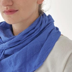 K&ouml;nnte beinhalten: Nahaufnahme eines blauen Schals, der um den Hals drapiert ist. Der Schal hat einen leuchtenden Blauton und scheint aus einem weichen, strukturierten Stoff zu bestehen. Der Hintergrund ist ein schlichtes Wei&szlig;, das die Farbe und Textur des Schals hervorhebt.