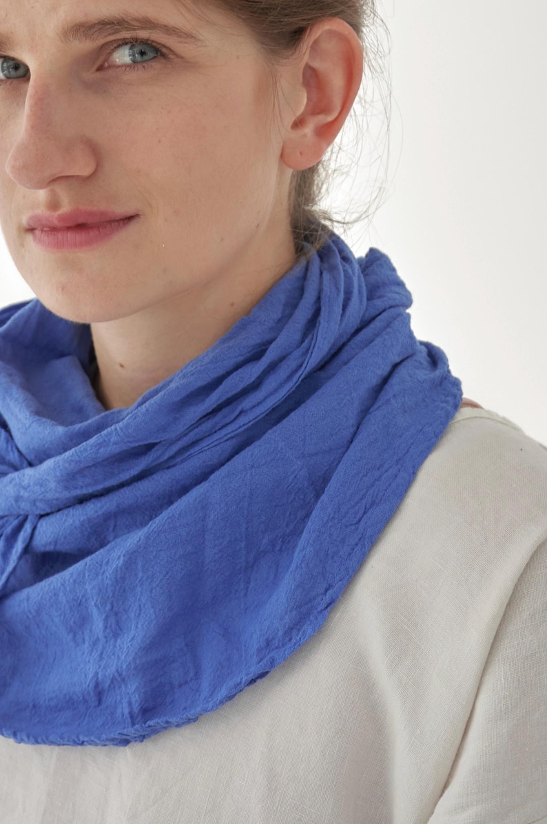 K&ouml;nnte beinhalten: Nahaufnahme eines blauen Schals, der um den Hals drapiert ist. Der Schal hat einen leuchtenden Blauton und scheint aus einem weichen, strukturierten Stoff zu bestehen. Der Hintergrund ist ein schlichtes Wei&szlig;, das die Farbe und Textur des Schals hervorhebt.