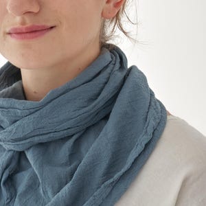 K&ouml;nnte beinhalten: Nahaufnahme eines blauen Schals, der um den Hals drapiert ist. Der Schal hat ein strukturiertes Aussehen und besteht aus einem weichen Material. Die Person tr&auml;gt ein wei&szlig;es Hemd.