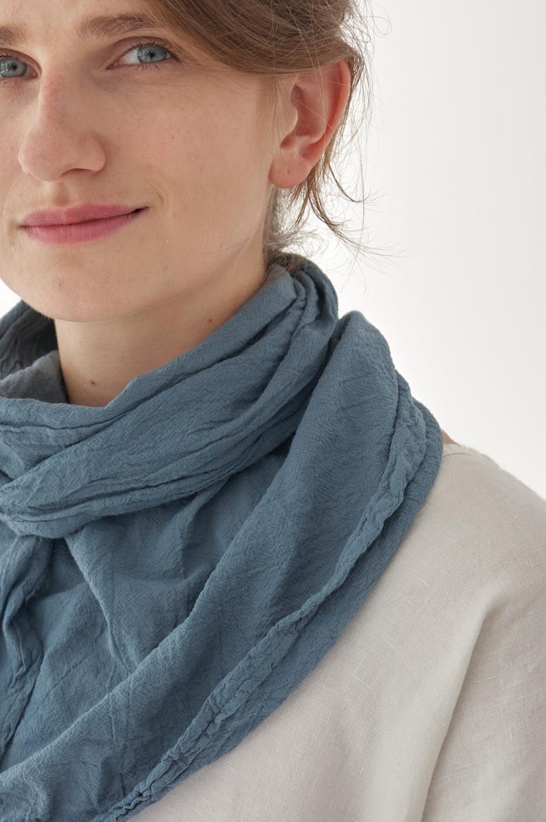 K&ouml;nnte beinhalten: Nahaufnahme eines blauen Schals, der um den Hals drapiert ist. Der Schal hat ein strukturiertes Aussehen und besteht aus einem weichen Material. Die Person tr&auml;gt ein wei&szlig;es Hemd.