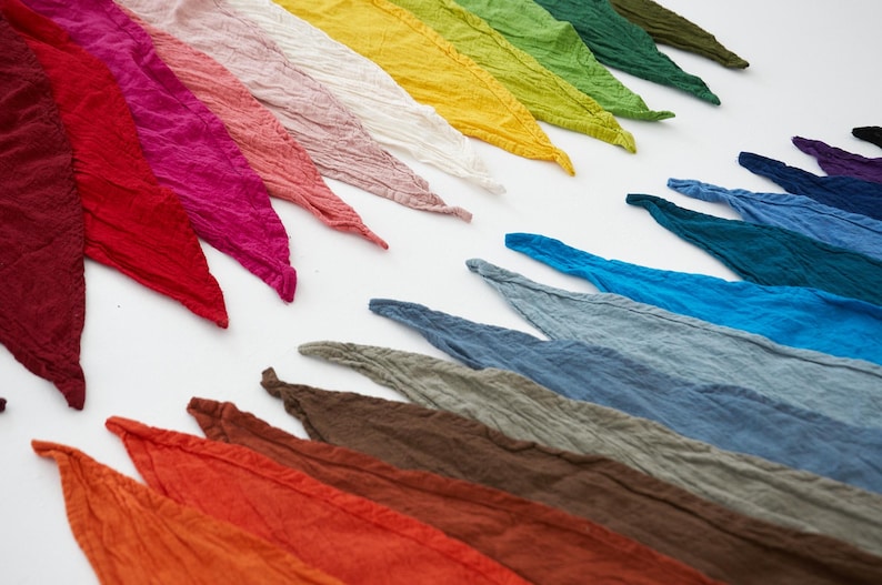 K&ouml;nnte beinhalten: Eine Sammlung farbenfroher, strukturierter Schals, die in Reihen angeordnet sind. Die Schals zeigen ein Farbspektrum, darunter Rot-, Rosa-, Gelb-, Gr&uuml;n-, Blau- und Braunt&ouml;ne. Der Stoff scheint leicht und leicht zerknittert zu sein.