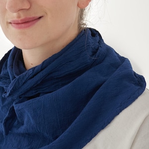 K&ouml;nnte beinhalten: Nahaufnahme einer Person, die einen dunkelblauen Schal tr&auml;gt. Der Schal besteht aus einem strukturierten Stoff und ist um den Hals drapiert. Die Person tr&auml;gt ein helles Hemd.