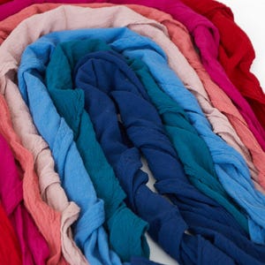 K&ouml;nnte beinhalten: Eine Anordnung farbiger Stoffstreifen in Rot-, Rosa-, Blau- und T&uuml;rkist&ouml;nen. Die Stoffe sind in einem Bogen angeordnet und scheinen eine Textur zu haben, m&ouml;glicherweise Leinen oder Baumwolle.