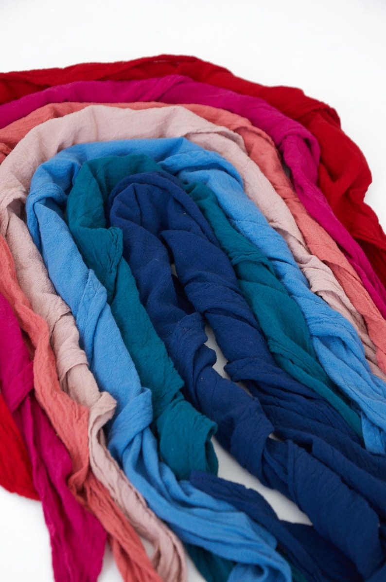 K&ouml;nnte beinhalten: Eine Anordnung farbiger Stoffstreifen in Rot-, Rosa-, Blau- und T&uuml;rkist&ouml;nen. Die Stoffe sind in einem Bogen angeordnet und scheinen eine Textur zu haben, m&ouml;glicherweise Leinen oder Baumwolle.