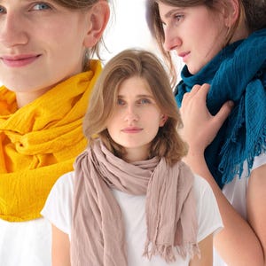 May include: A woman wearing a light pink scarf, a yellow scarf, and a teal scarf. The scarves are made of a soft, textured fabric. The woman is wearing a white t-shirt.