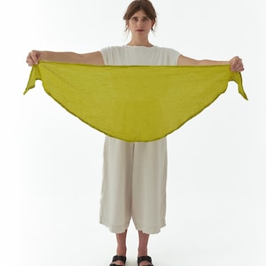 K&ouml;nnte beinhalten: Eine Frau h&auml;lt einen chartreusefarbenen Schal. Der Schal hat eine dreieckige Form und eine leicht strukturierte Optik. Sie tr&auml;gt ein wei&szlig;es T-Shirt, beige Culottes und schwarze Sandalen. Der Hintergrund ist schlicht wei&szlig;.