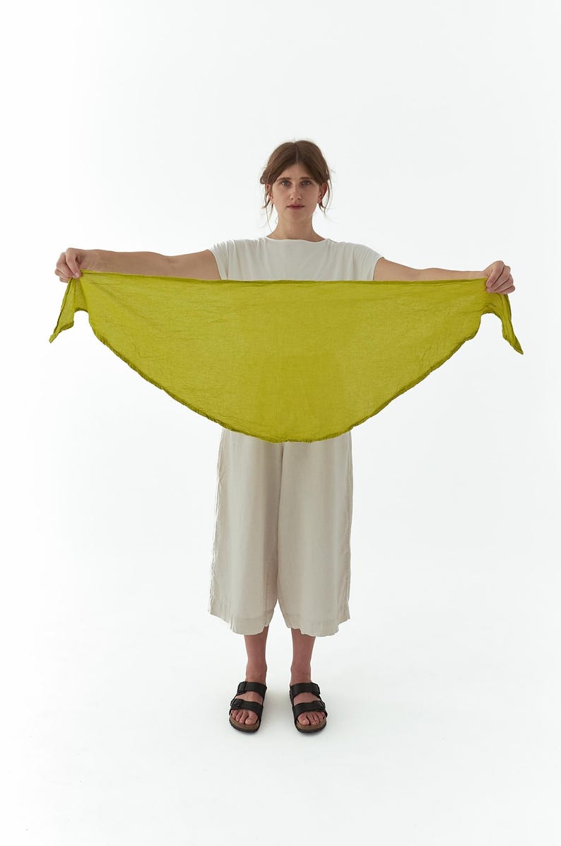 K&ouml;nnte beinhalten: Eine Frau h&auml;lt einen chartreusefarbenen Schal. Der Schal hat eine dreieckige Form und eine leicht strukturierte Optik. Sie tr&auml;gt ein wei&szlig;es T-Shirt, beige Culottes und schwarze Sandalen. Der Hintergrund ist schlicht wei&szlig;.