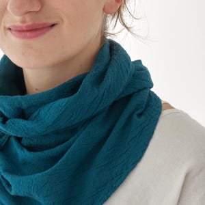 K&ouml;nnte beinhalten: Ein t&uuml;rkisfarbener Schal aus strukturiertem Stoff ist um den Hals drapiert. Der Schal steht im Mittelpunkt, darunter ist ein helles Oberteil zu sehen. Das Bild ist eine Nahaufnahme, die die Farbe und Textur des Schals hervorhebt.